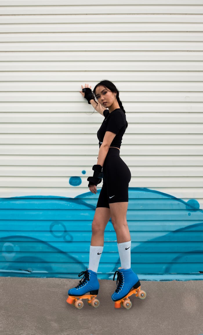 Stylish woman in activewear poses on roller skates in front of a metal shutter with blue graffiti art.